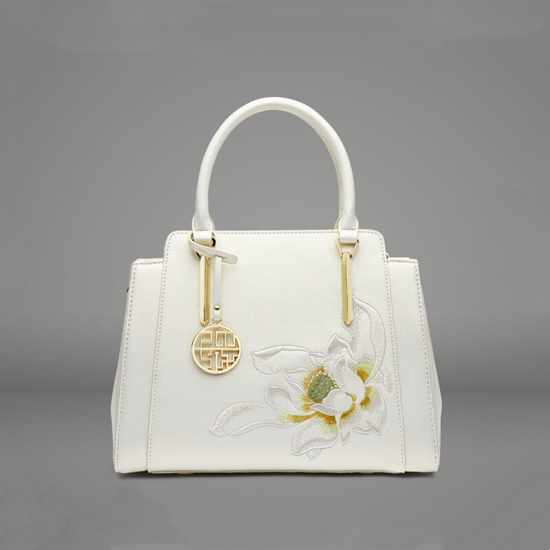 White handbag with floral design and gold accents on a gray background