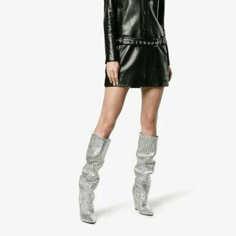 Person wearing a black leather outfit with silver high boots on a white background