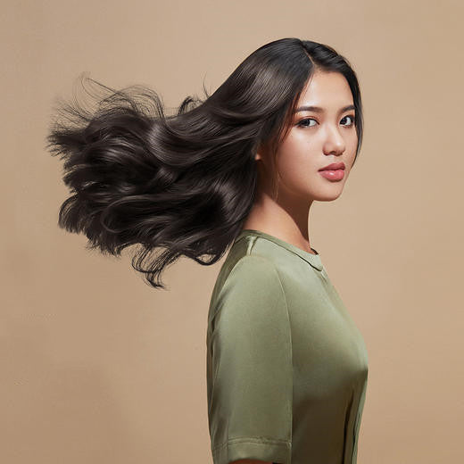 Woman with flowing dark hair wearing a green shirt against a beige background