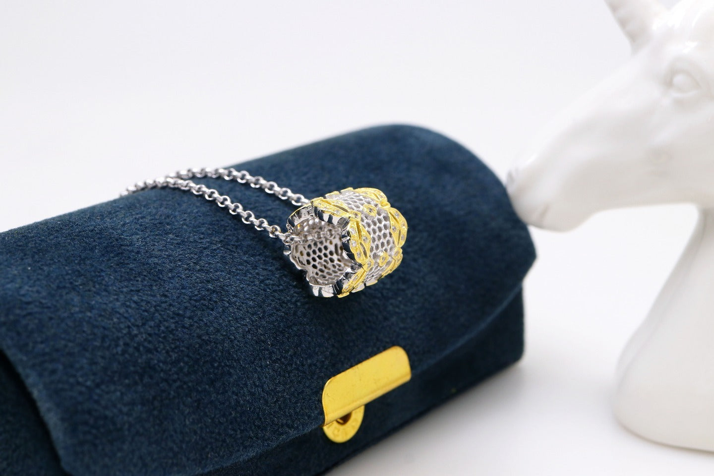 Gold and silver bracelet on a blue cushion with a white decorative object in the background