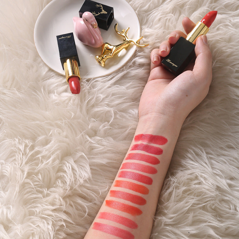 Hand holding a red lipstick with swatches on a arm, on a fluffy white surface.