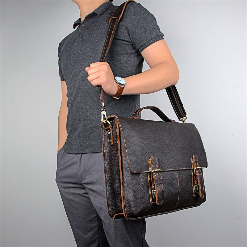 Person holding a dark brown leather briefcase against a gray background