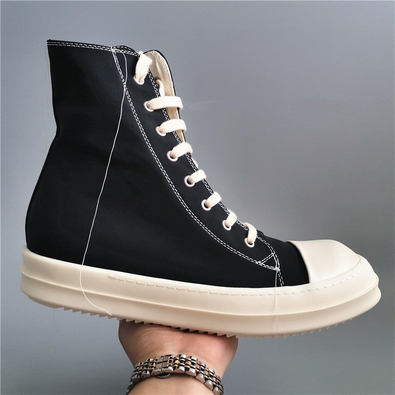 Black high-top sneaker with white laces and sole held by a hand against a gray background