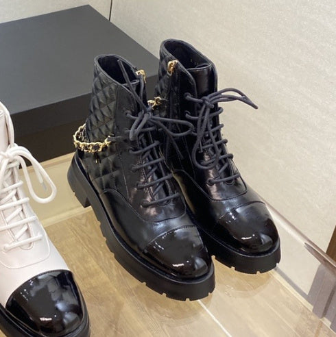 Black leather boots with gold chain details on a wooden floor.
