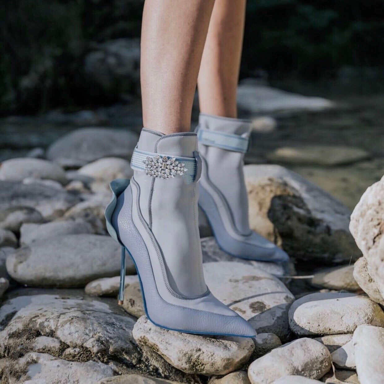 Gray high-heeled shoes with embellishments on a rocky surface