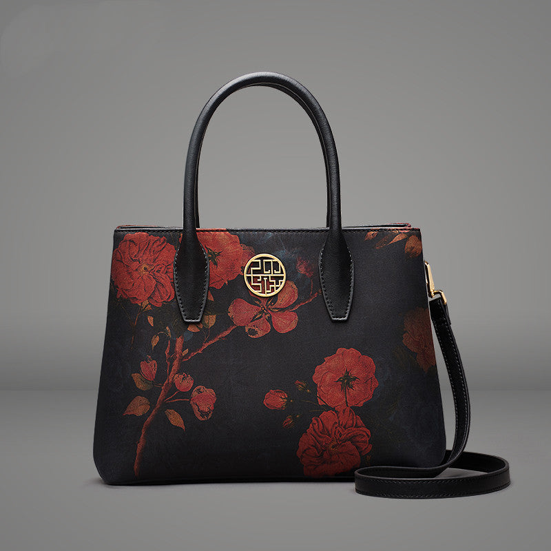 Black handbag with red floral patterns on a gray background
