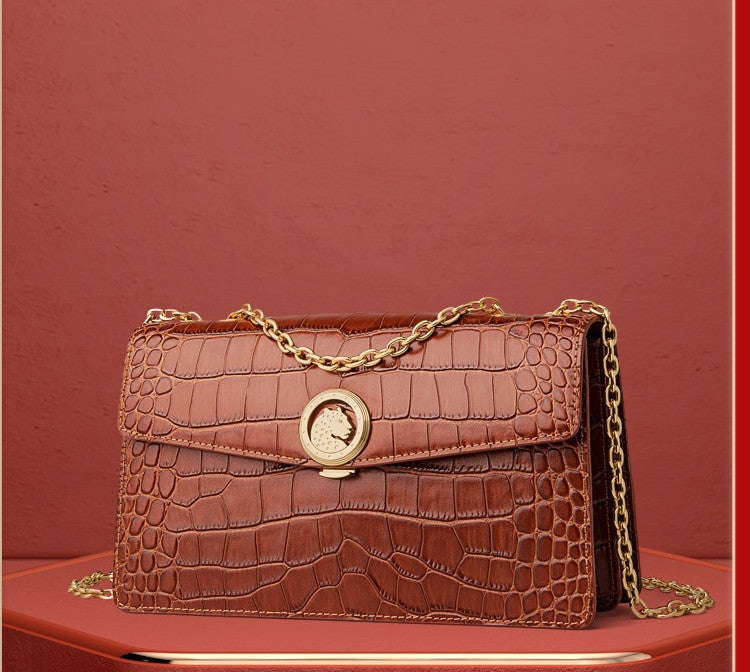 Brown crocodile-patterned handbag with a gold chain on a red background