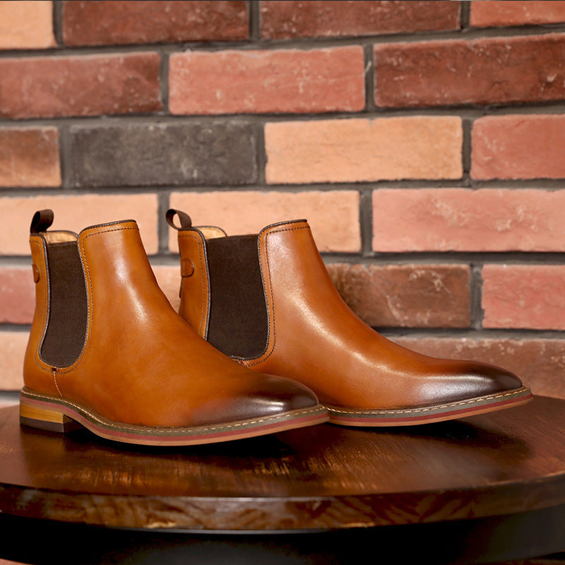 Pair of brown leather Chelsea boots on a wooden surface with a brick wall background