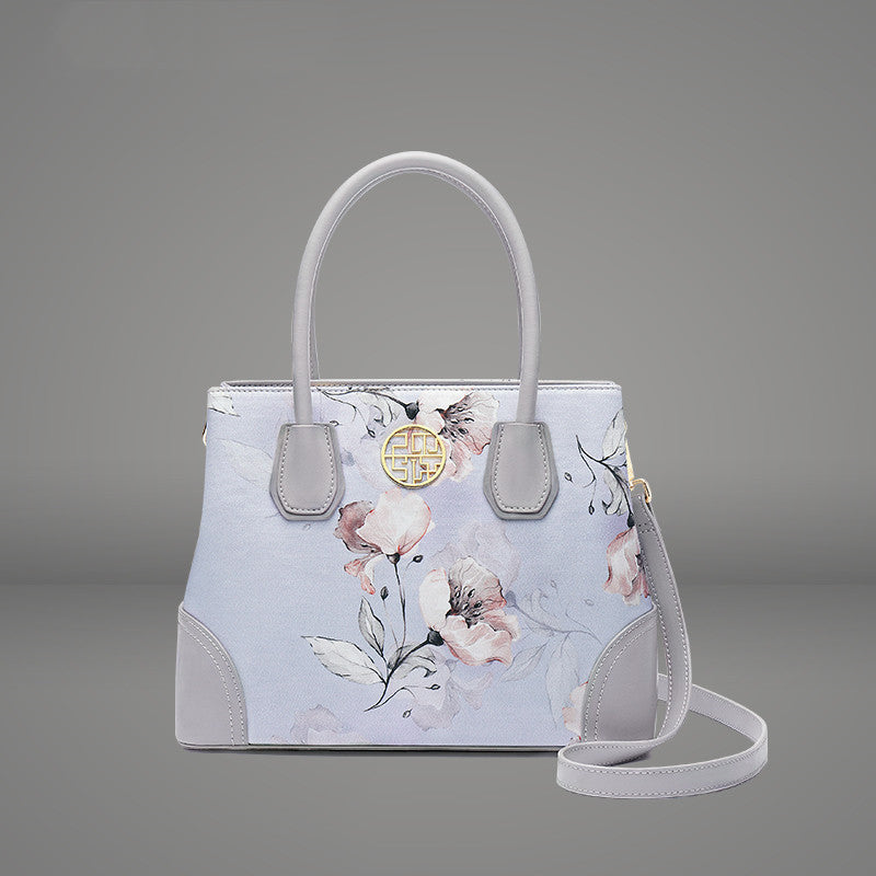 Handbag with floral design and gold emblem on a gray background