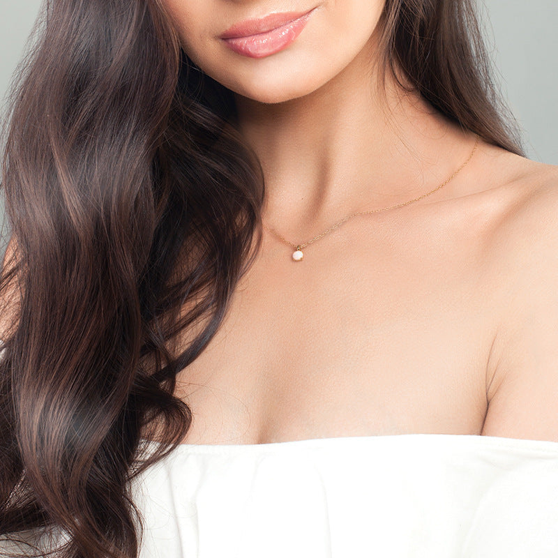 Close-up of a woman wearing a delicate necklace with a small pendant against a neutral background