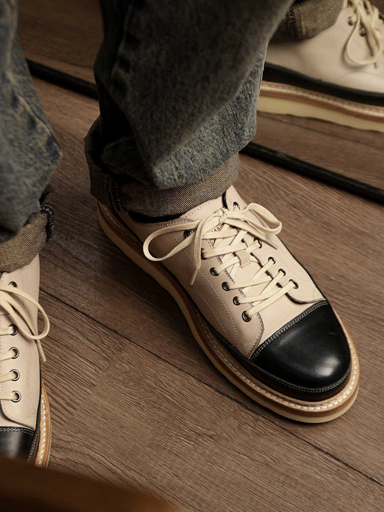 Close-up of a person wearing beige sneakers with black toes on a wooden floor.