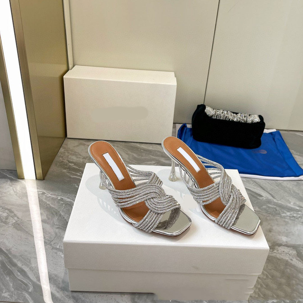 Pair of silver high-heeled sandals on a white box with a neutral background