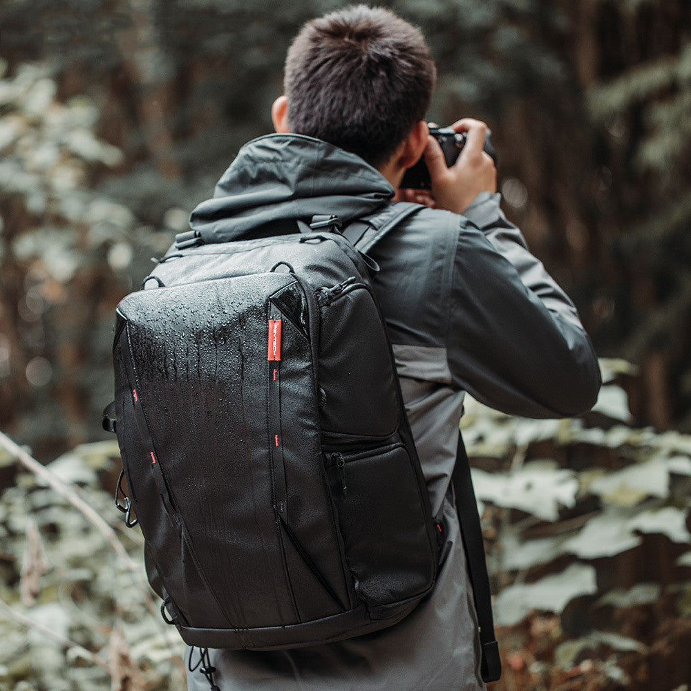 Person taking a photo in a forest with a black backpack