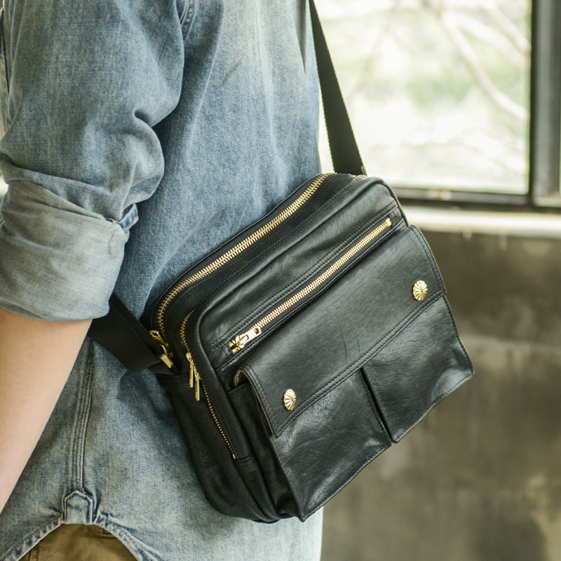 Person wearing a black leather crossbody bag with gold zippers.