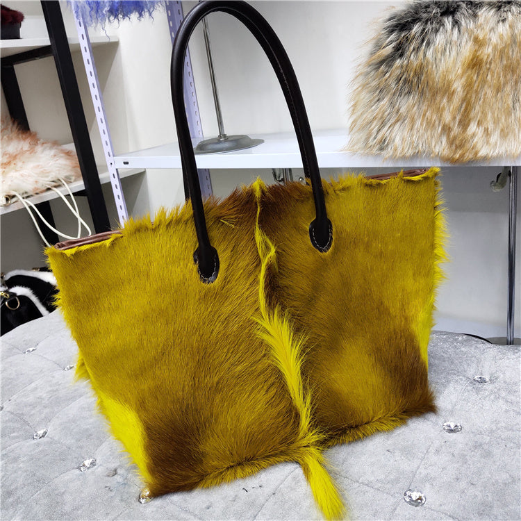 Yellow fur tote bag with black handles on a gray surface