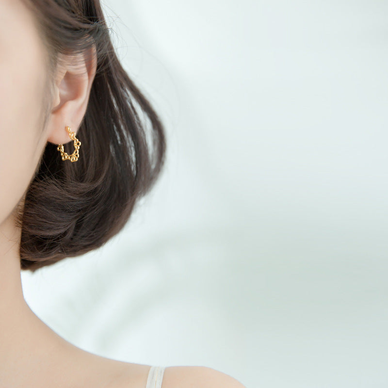 Close-up of a gold earring worn by a person with a plain background