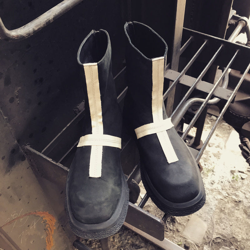 Black rain boots with white straps hanging on a metal structure.