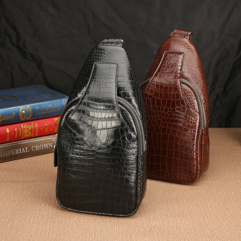 Two crocodile-patterned sling bags, one black and one brown, on a textured surface with books in the background.