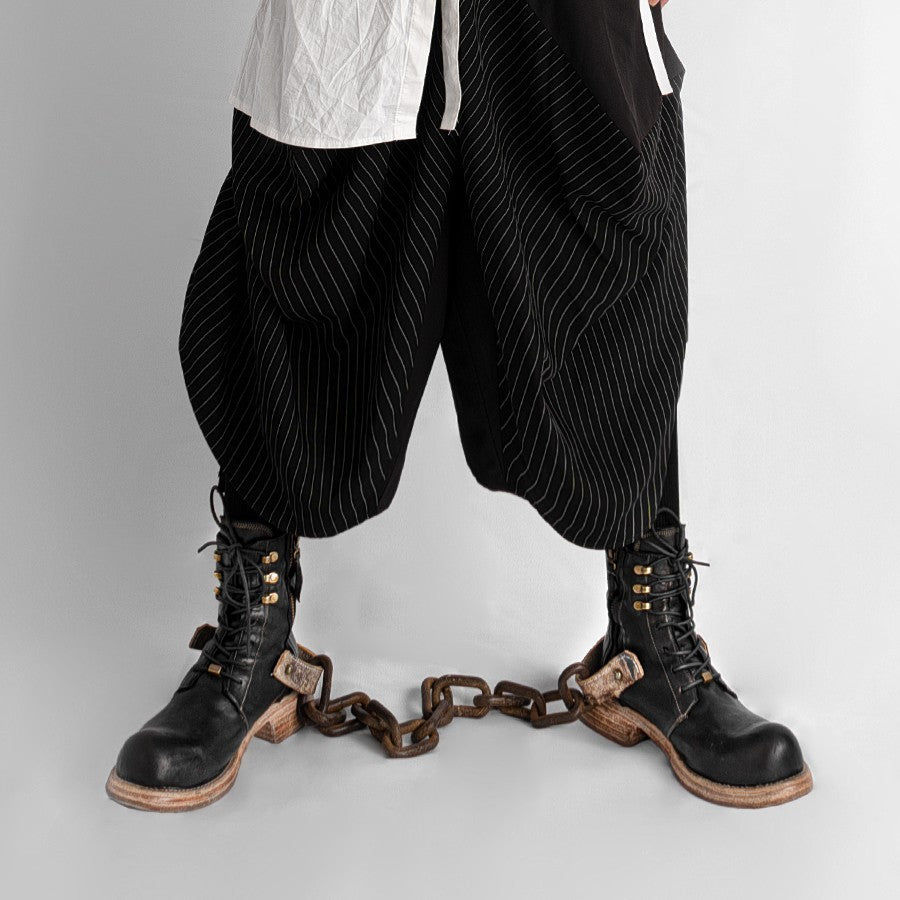 Person wearing black pinstripe pants and black boots with chains on a gray background