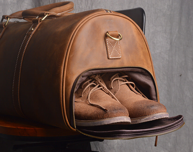 Brown leather duffel bag with open zipper showing brown boots on a gray background