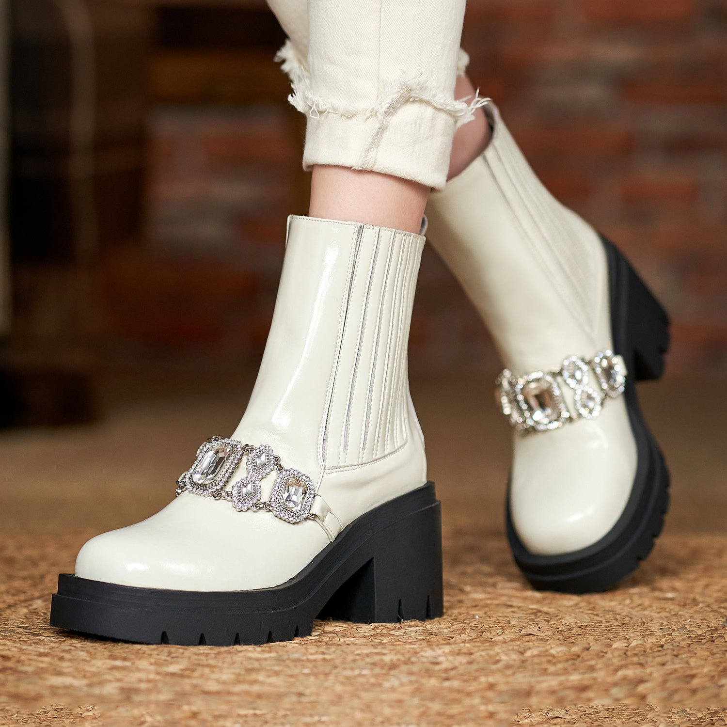 White boots with black soles and silver buckles worn by a person on a wooden floor.