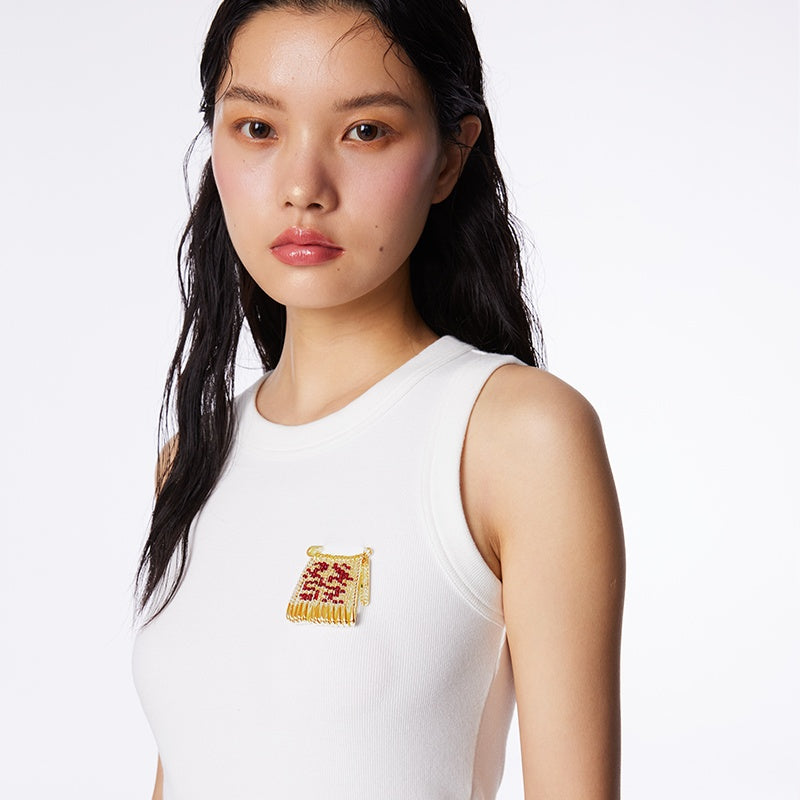 Woman wearing a white sleeveless top with a decorative patch on a plain background