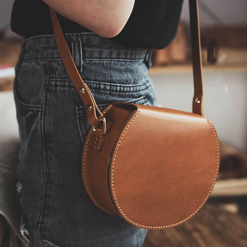 Brown leather handbag worn over shoulder with blurred background