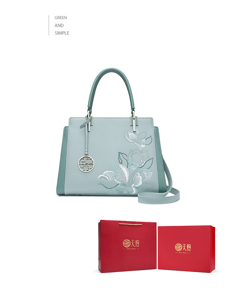 Light blue handbag with floral embroidery and matching red box on a white background