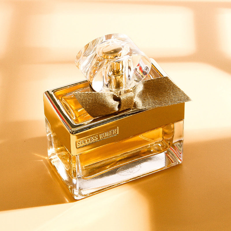 Gold and clear perfume bottle with a bow on a warm beige background