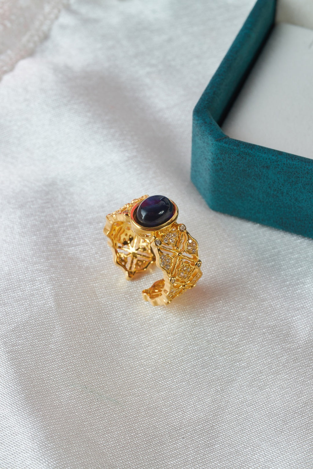 Gold ring with a dark gemstone on a white fabric background