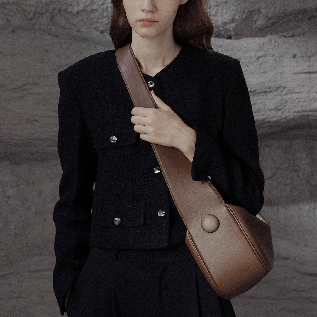 Person wearing a black coat holding a brown leather bag against a textured wall.