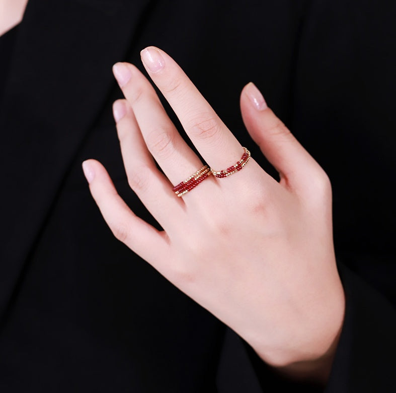 Hand wearing a red beaded ring against a black background