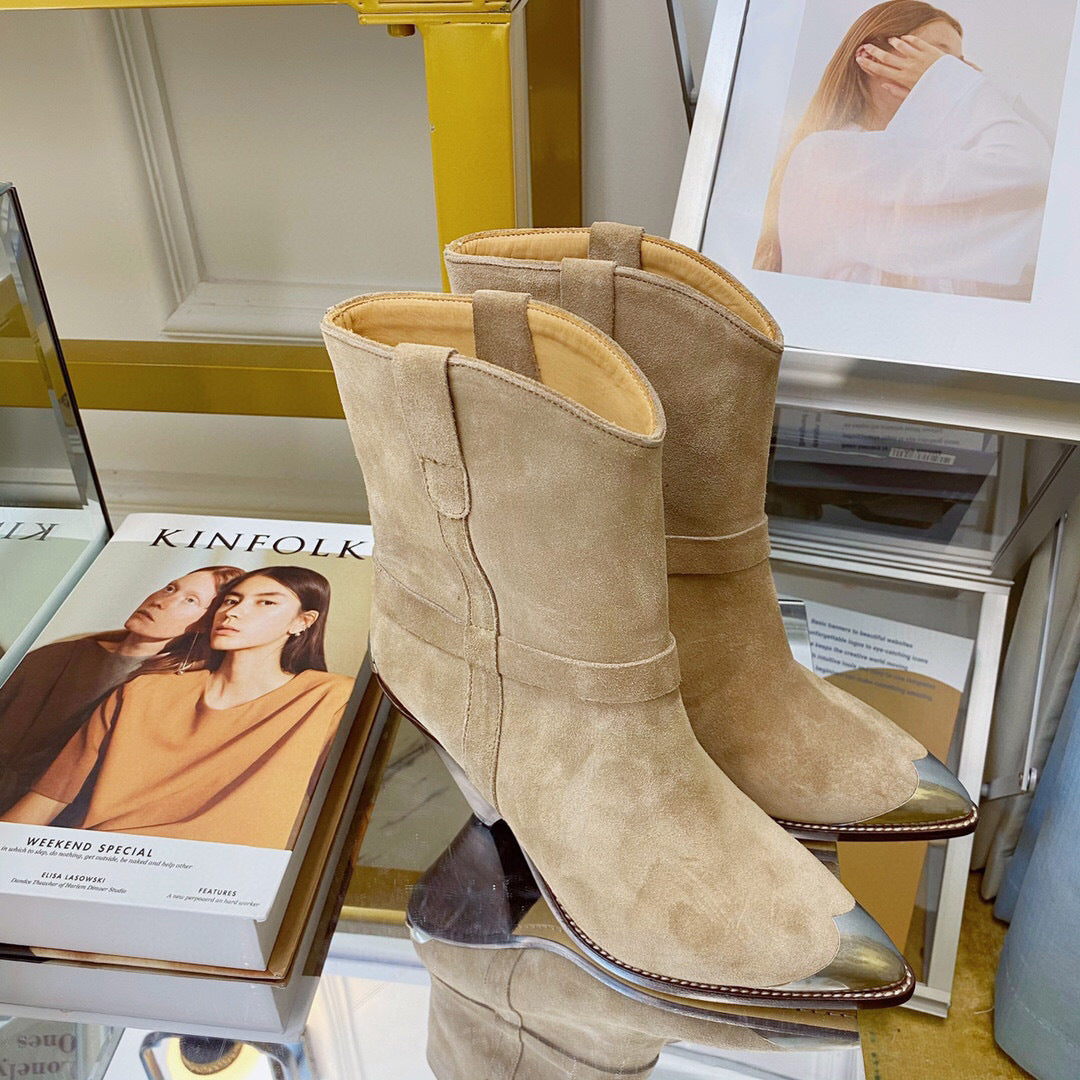 Pair of beige suede boots on a surface with books and a magazine in the background