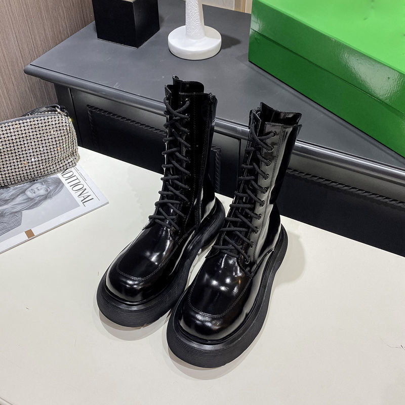 Black leather boots on a white surface with a magazine and green box in the background.