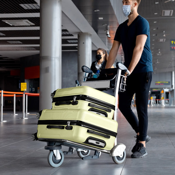 Person with a face mask pushing a cart with suitcases in an airport terminal.