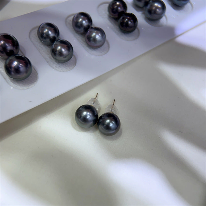 Pair of black pearl earrings on a white surface with more pearls in the background.
