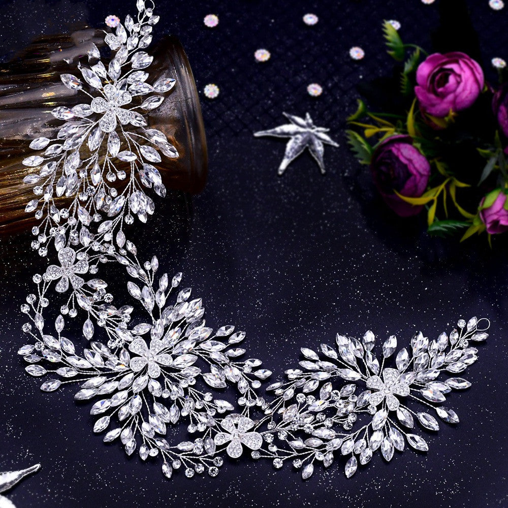 Silver floral hair vine on a dark surface with flowers and a bottle.