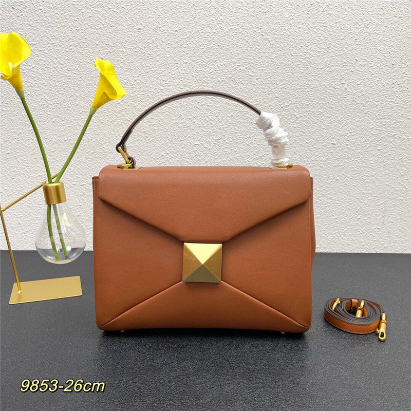 Brown handbag with gold accents on a dark surface, with yellow flowers and a decorative light bulb in the background.