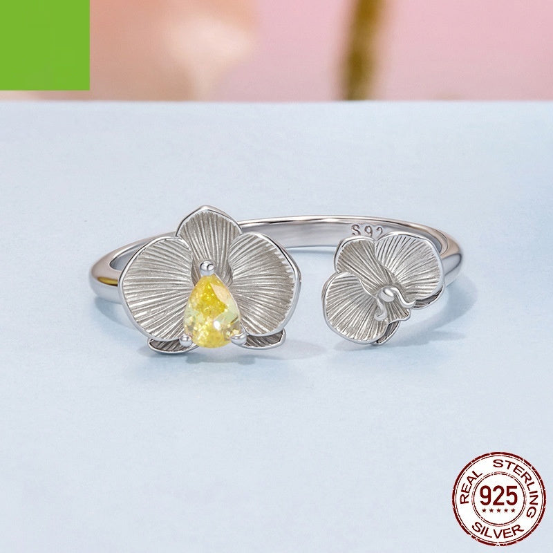 Silver ring with floral design and yellow gemstone on a light blue background