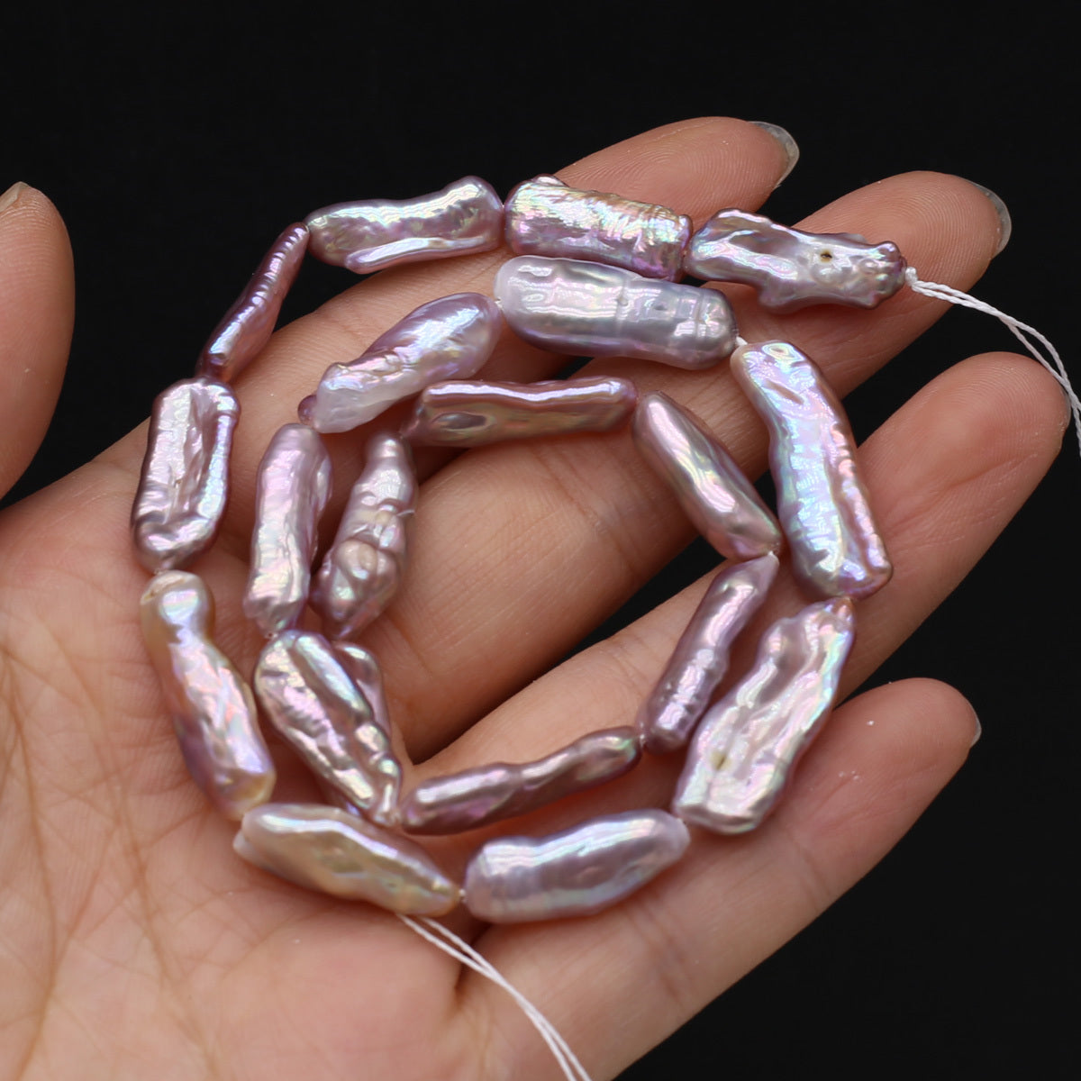 String of pink freshwater pearls held in a hand against a black background