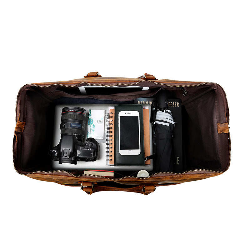 Open brown leather duffel bag with camera, phone, and other items on a white background