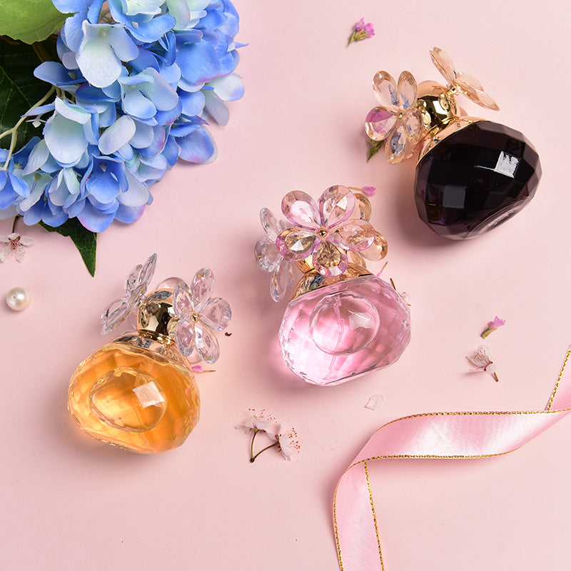 Three perfume bottles with decorative caps on a pink background with flowers and a ribbon.