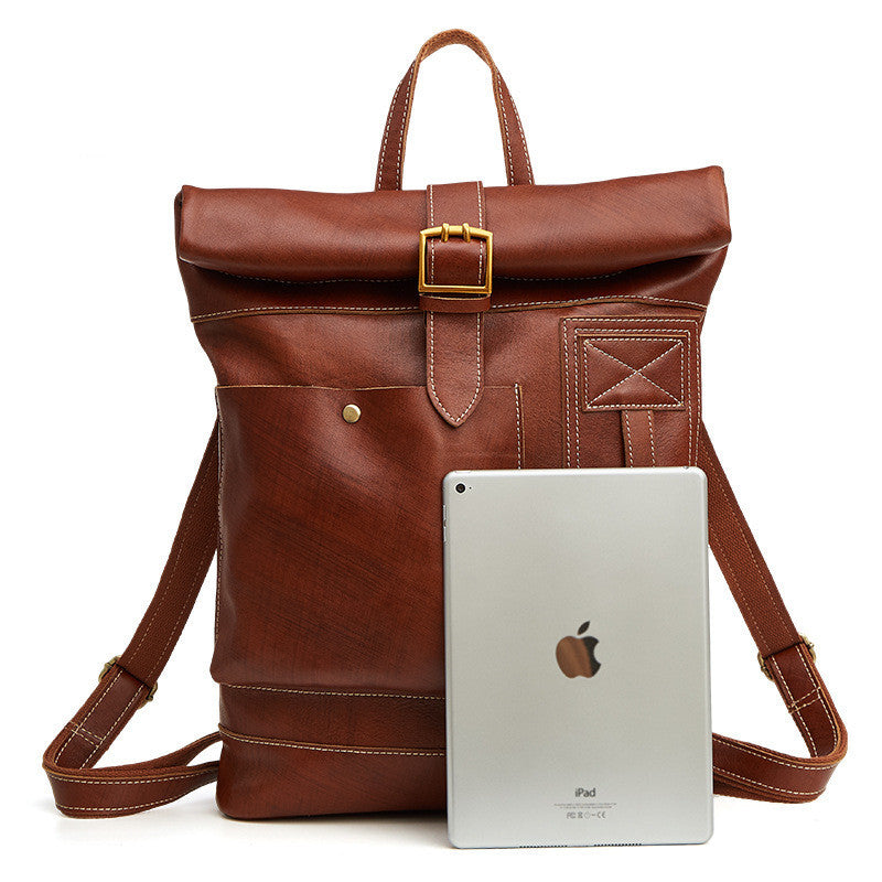 Brown leather backpack with a gold buckle next to an Apple iPad on a white background