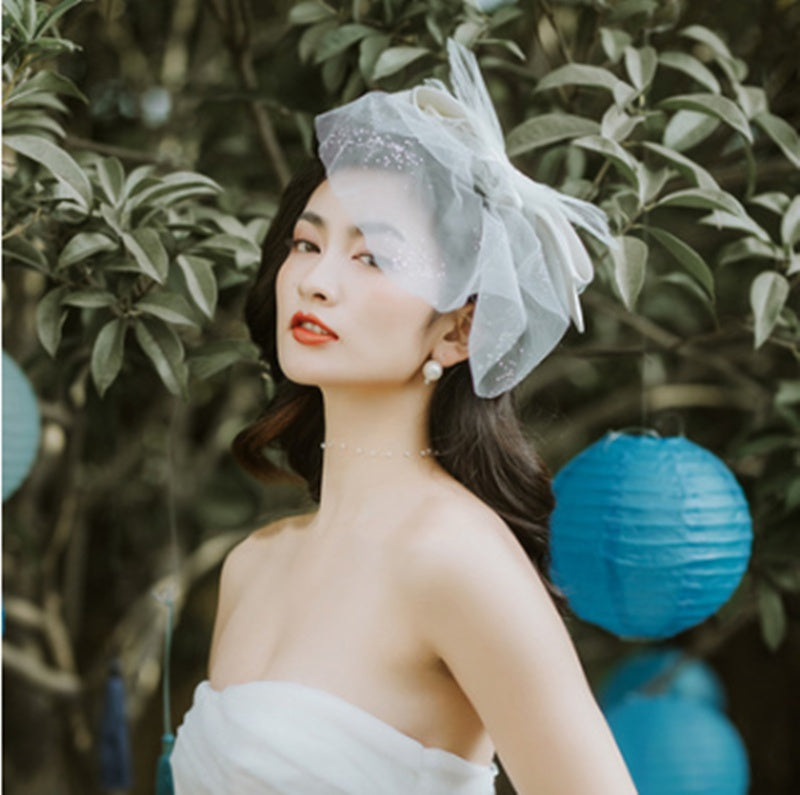 Woman wearing a decorative headpiece with green foliage and blue lanterns in the background