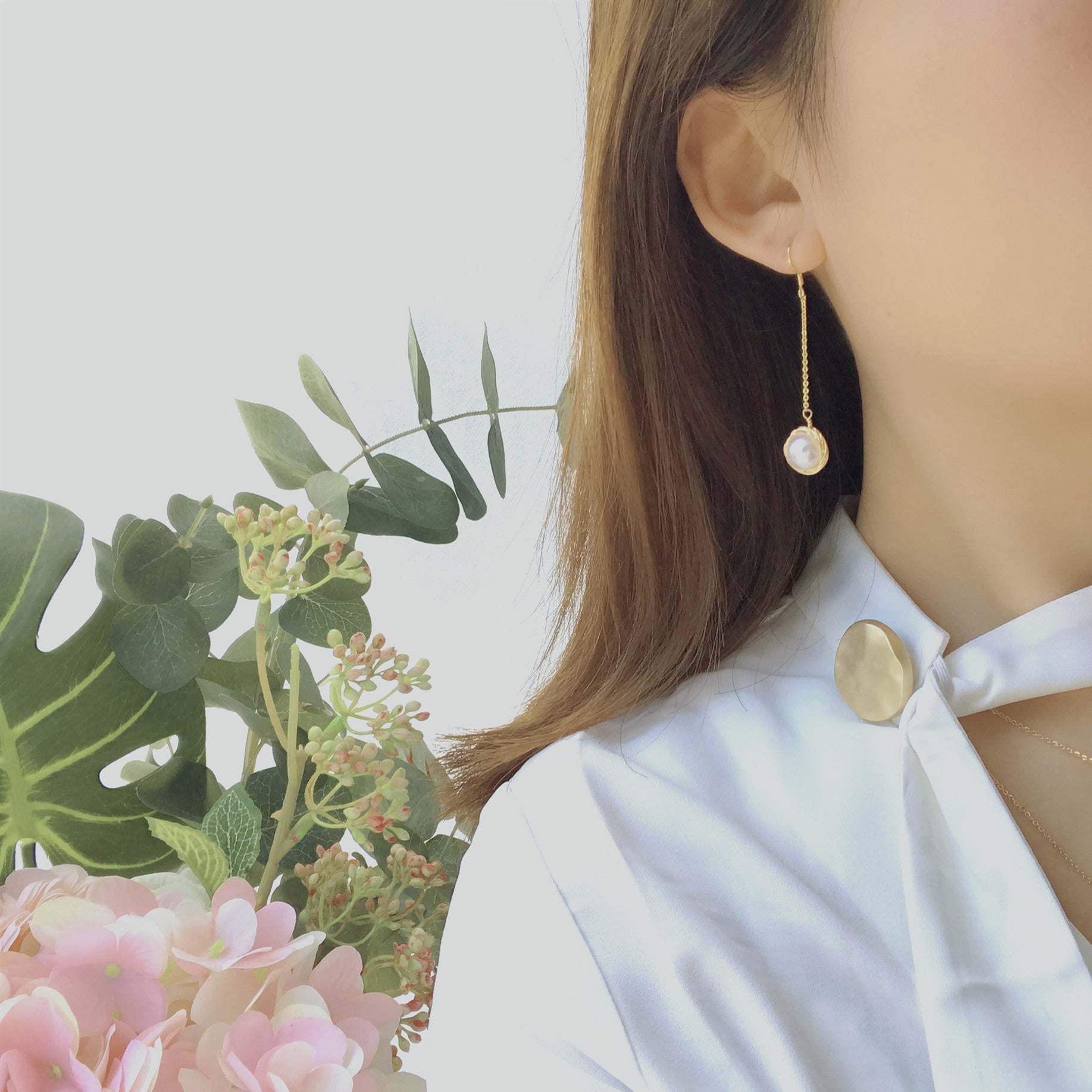 Pearl earring worn by a person with a blurred background of flowers and greenery
