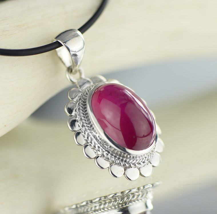Silver pendant with a pink stone on a reflective surface