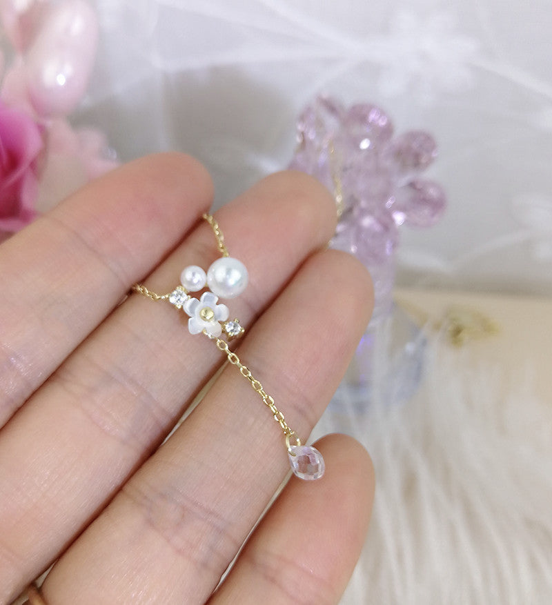 Delicate gold chain with pearls and crystals held between fingers against a soft floral background