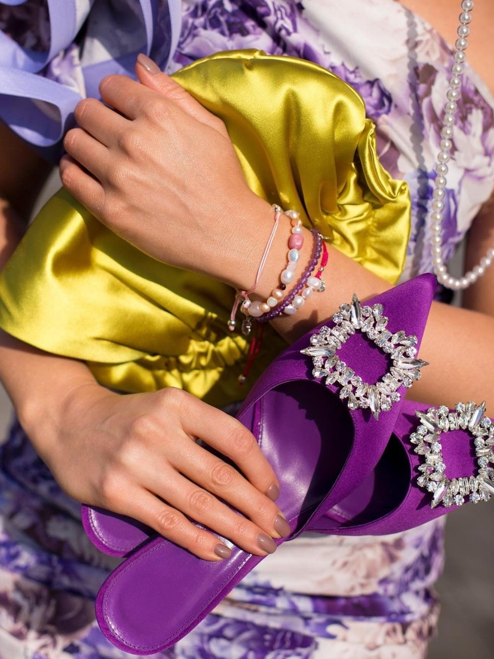 Purple sandals with decorative straps worn by a person holding a yellow satin bag.