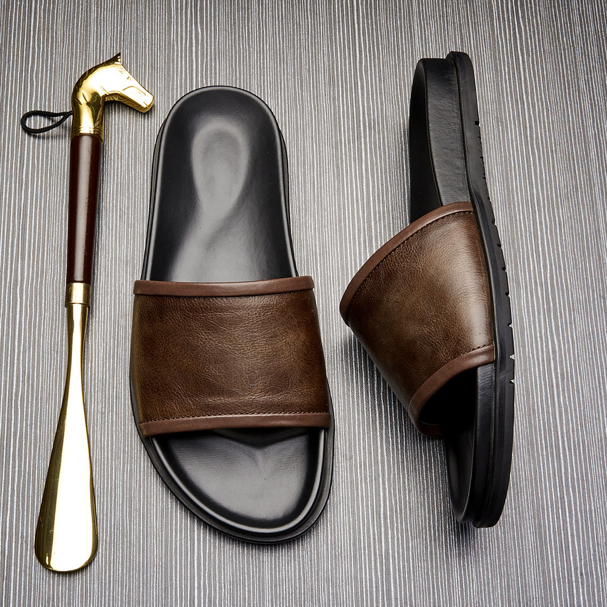 Brown leather slide sandals with a gold shoe horn on a textured surface