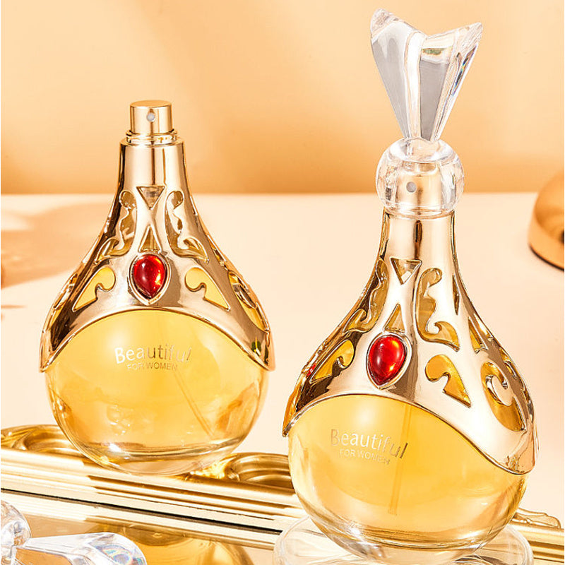 Two ornate perfume bottles with gold accents and red gemstones on a reflective surface.